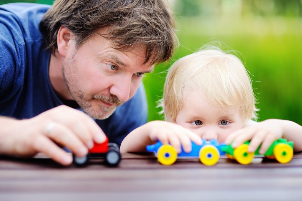 Middle age father and his toddler son playing with toy trains outdoors